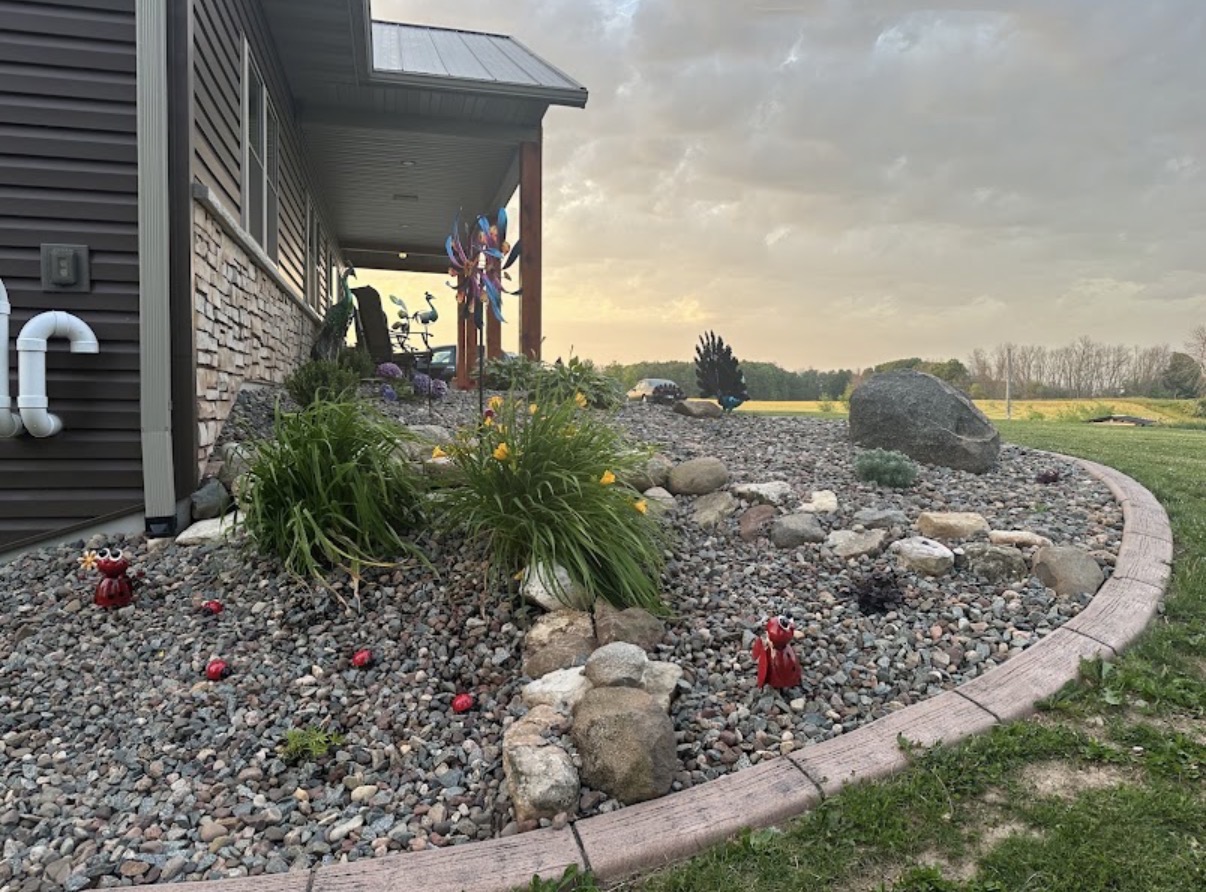 Curved rock bed with boulders and fresh plantings along a home